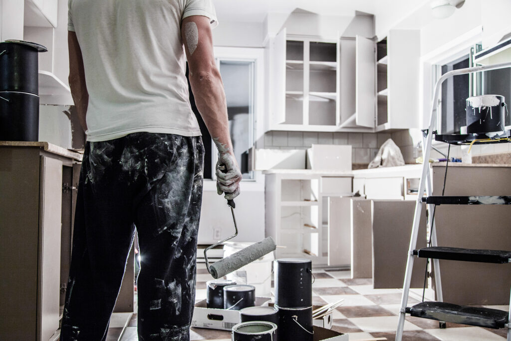 alt="a-man-standing-with-a-painting-brush-renovating-the-kitchen-section-of-a-rental-home"