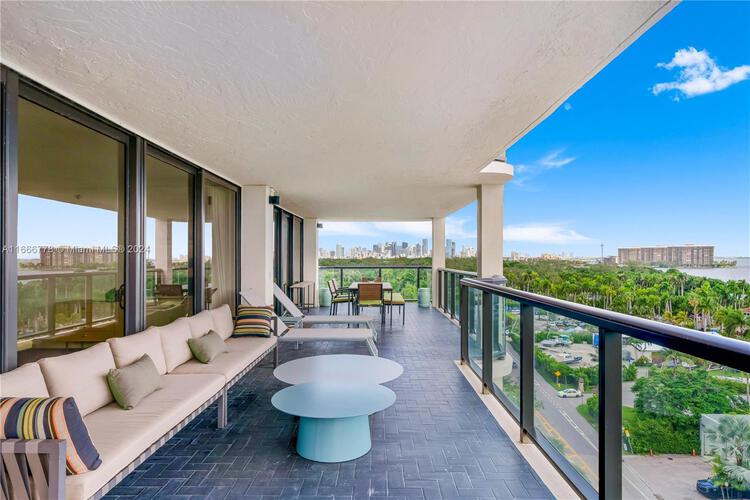 Spacious covered balcony with lounge seating and table overlooking Coconut Grove skyline and Biscayne Bay.
