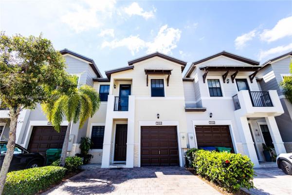 Front view of modern Doral townhomes with paired garages, balconies, and tropical landscaping.

