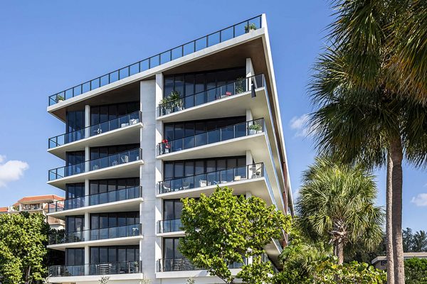 Exterior view of a modern six‑story Fairchild condominium building framed by palm trees under a clear blue sky.
