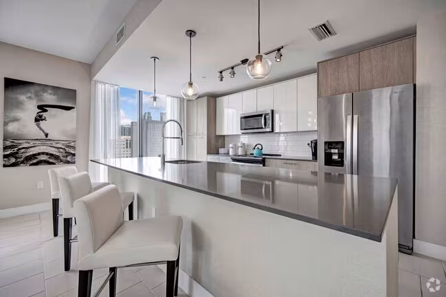 Modern Downtown Miami kitchen with a long waterfall island, stainless‑steel appliances, and barstool seating.
