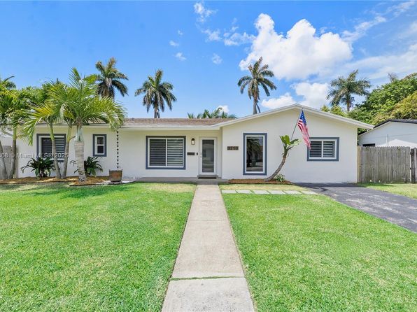 Front view of a white-painted single-family home in Cutler Bay with large lawn, paved walkway, palm trees, and American flag