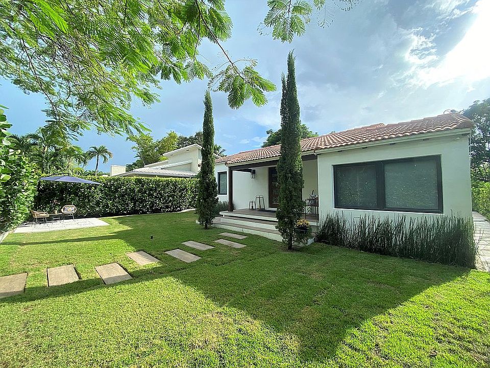 Charming one-story home with tile roof, manicured lawn, and tall greenery